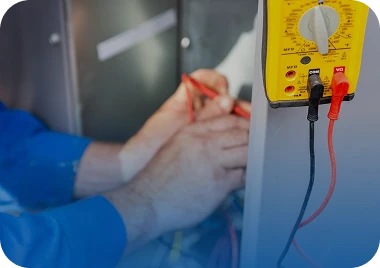 A technician in a blue shirt uses a red probe to test electrical wiring next to a yellow multimeter.