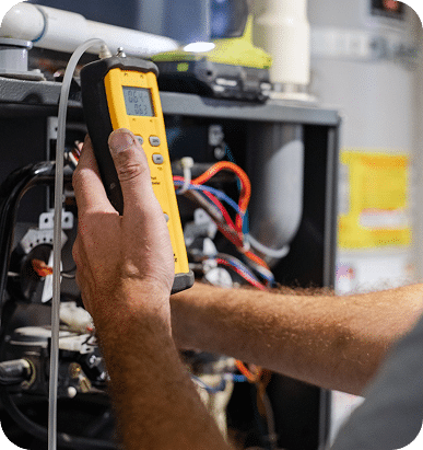 A person's hands hold a yellow diagnostic tool with "0.64" and "0.63" on the screen, connected to a furnace.