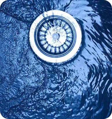 Water swirls around a shiny metal sink drain, creating ripples and reflections in a blue hue.