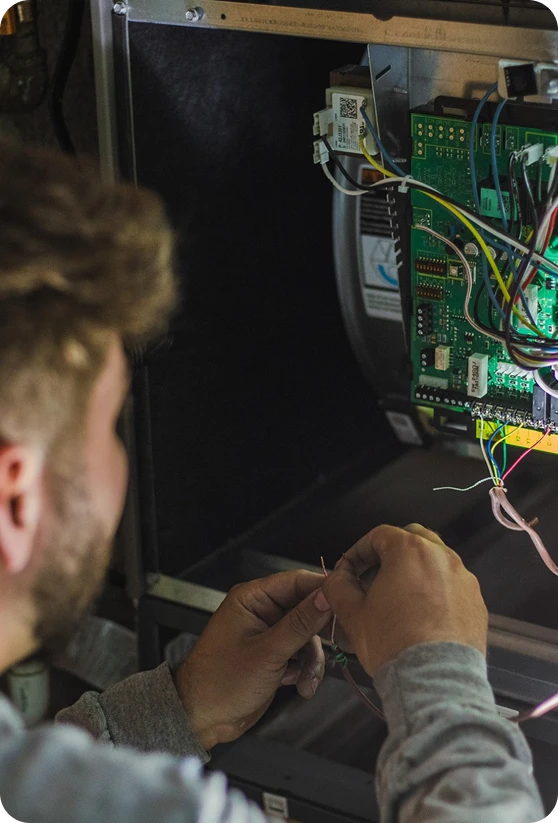 A man with a beard and gray shirt works on exposed wires near a circuit board with many colorful wires.