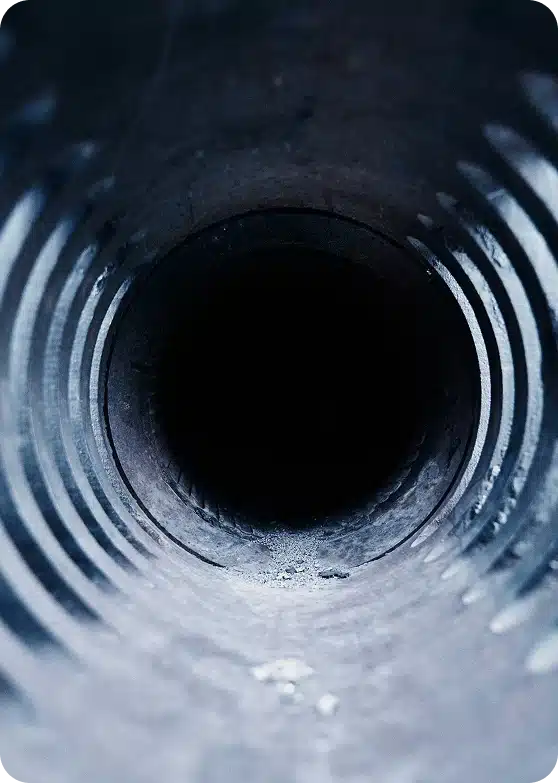 Looking down a dark, textured pipe with a black hole at the center and light reflecting off the edges.