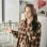 A woman in a plaid shirt talks on a phone, gesturing towards white water heaters and pipes.