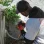 A person in a gray cap and orange gloves uses pliers to work on electrical wires near an AC unit.