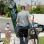 A man in a gray shirt and black cap carries a green ladder and equipment, walking away from a "Family plan" van.